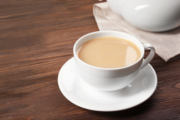White cup filled with light brown milk coffee on a matching saucer, placed on a wooden table