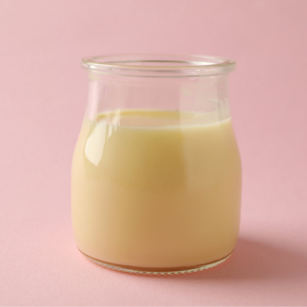 Small glass jar filled with light-yellow coconut condensed milk on a pink background