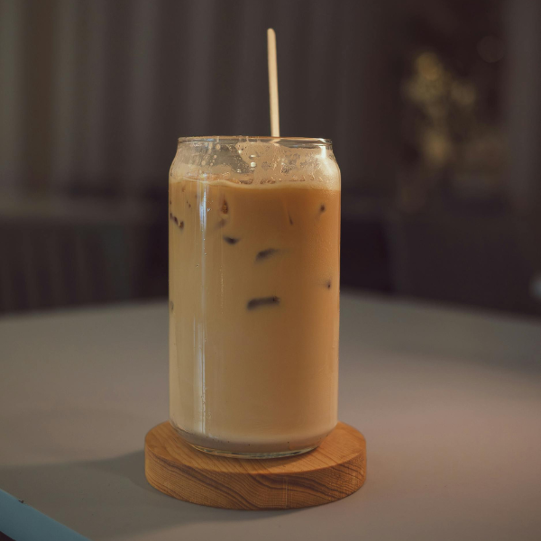 A tall glass of creamy Vietnamese coconut iced coffee with a straw, served on a wooden coaster in a softly lit setting