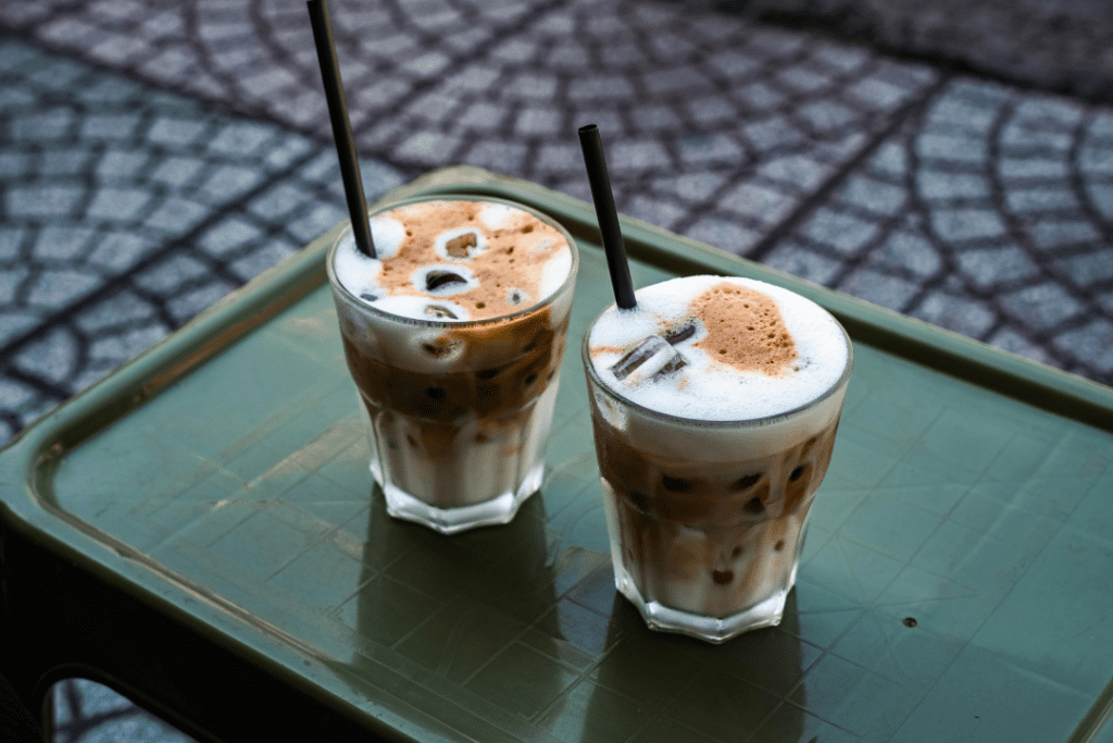 Two iced coffees topped with frothy foam, served in short glasses with straws on an outdoor table