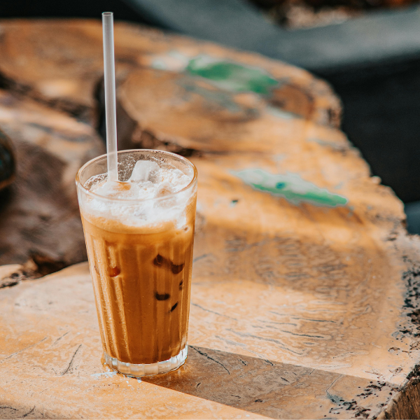 A tall glass of Vietnamese iced coffee with instant coffee with a straw on a rustic outdoor table